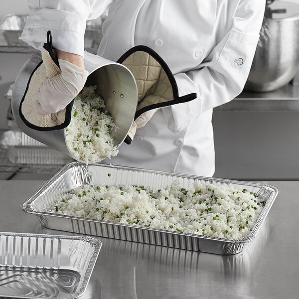 A chef pouring rice into a Choice heavy-duty foil steam table pan.