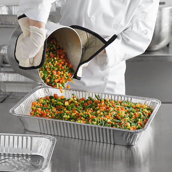 A chef using a Choice heavy-duty foil steam table pan to cook vegetables.