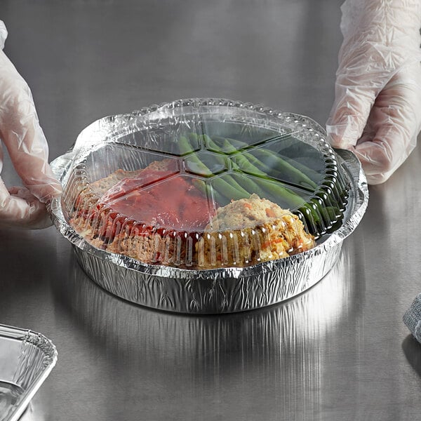 A gloved hand holding a Choice foil container with food inside.