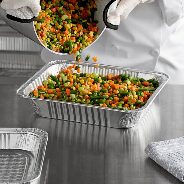 A chef pouring mixed vegetables into a Choice heavy-duty foil steam pan.
