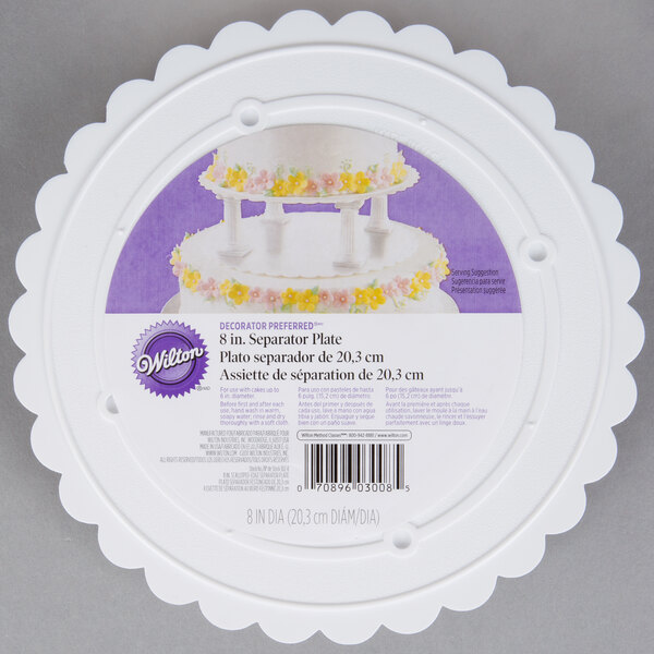 A white Wilton cake plate with a scalloped edge and flower design.