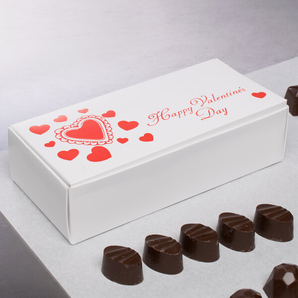 A white 1 lb. Valentine's Day candy box with red heart designs holding chocolates.