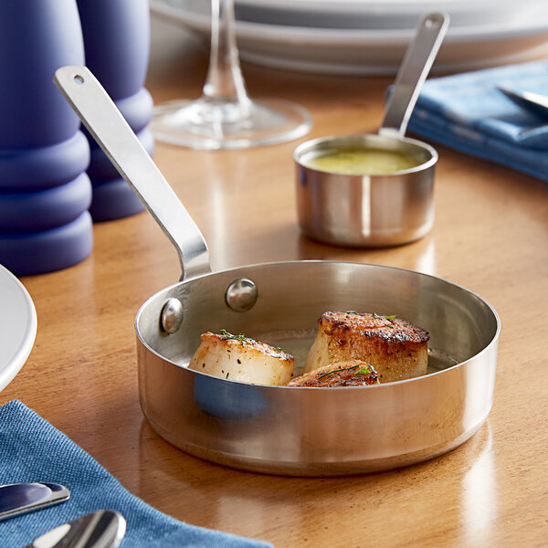 A Vollrath stainless steel sauce pan of scallops on a table.