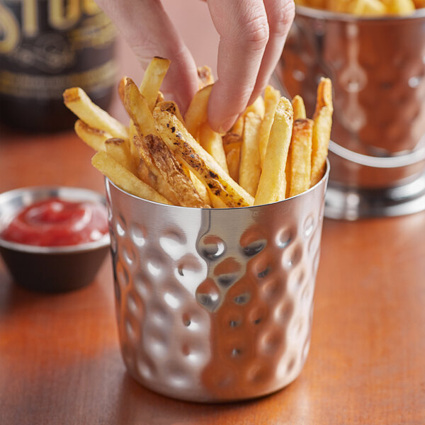 A person holding a Vollrath stainless steel cup of french fries.