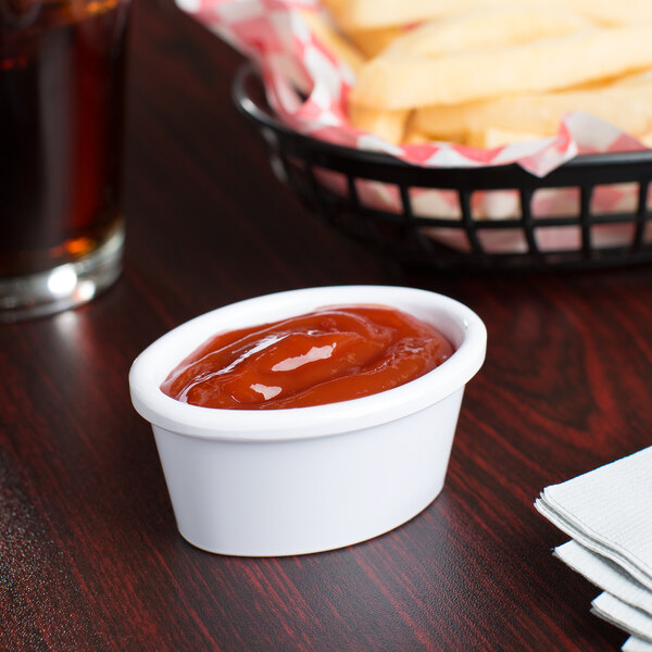 A table with a basket of French fries and Carlisle white oval ramekin filled with ketchup.