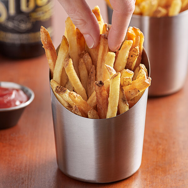 A person's hand taking a french fry out of a Vollrath stainless steel container.