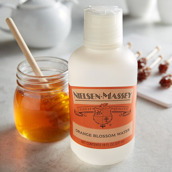 A close-up of a Nielsen-Massey Orange Blossom Water bottle next to a jar of honey.