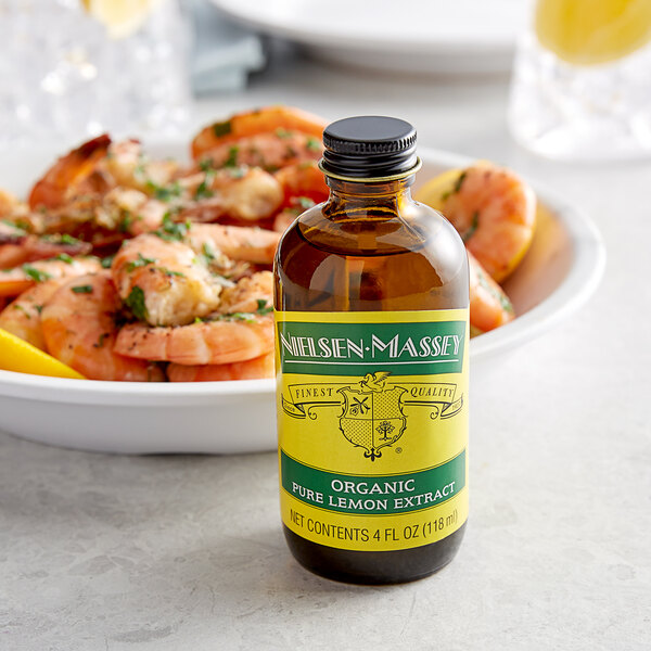 A close up of a Nielsen-Massey Pure Organic Lemon Extract bottle next to a bowl of shrimp.