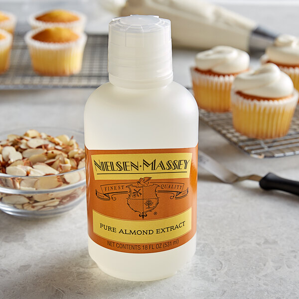 A bottle of Nielsen-Massey Pure Almond Extract next to a cupcake with white frosting.