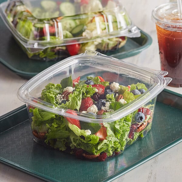 A Dart ClearPac SafeSeal plastic container filled with salad on a counter.