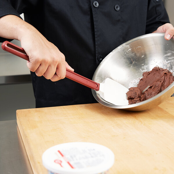 A hand using a red Vollrath SoftSpoon to mix brown dough in a bowl.