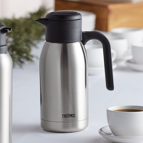 A silver and black stainless steel vacuum insulated carafe with coffee inside.