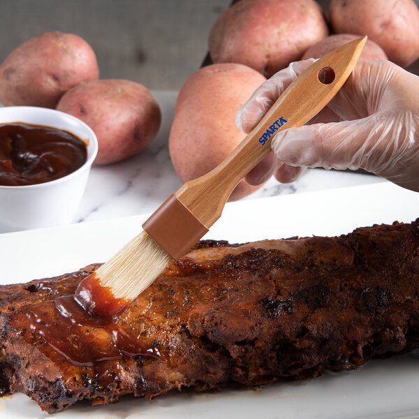 A person using a Carlisle boar bristle brush to baste meat on a table.