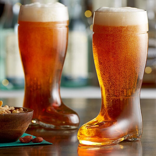 Two Stolzle beer boot glasses filled with beer on a table with a bowl of nuts.