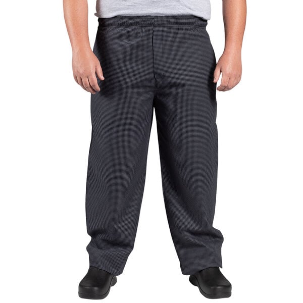 A man wearing black and gray houndstooth chef pants with his hands on his hips.
