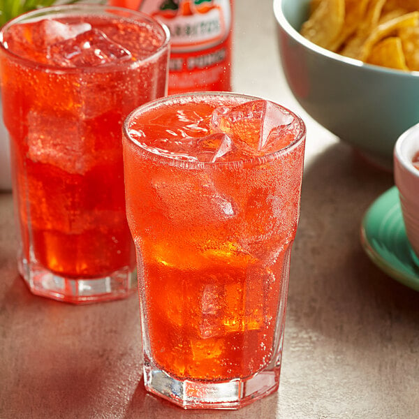 Two glasses of Jarritos Fruit Punch soda with ice on a table with chips.