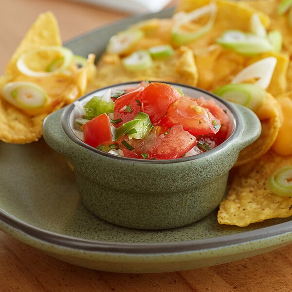 A moss green stoneware sauce cup filled with salsa on a plate.