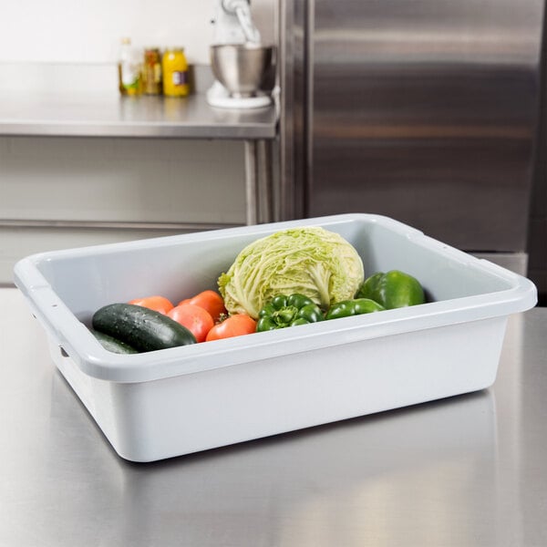 A gray Rubbermaid bus tub filled with vegetables on a counter.