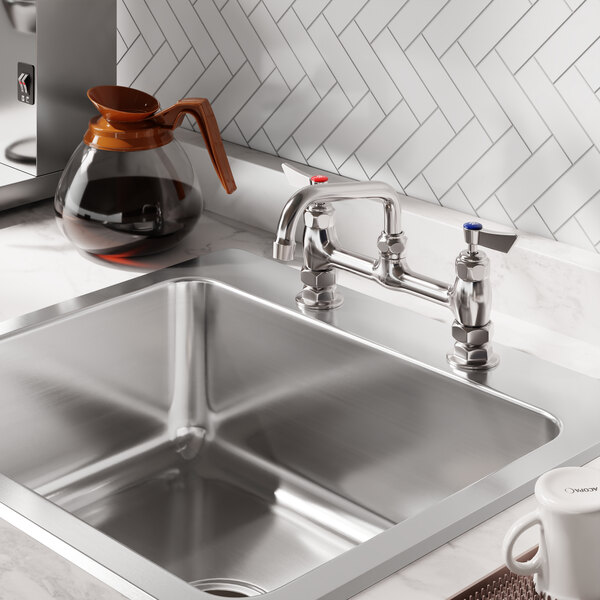 A stainless steel deck-mounted faucet with 8-inch centers and a 6-inch swing spout installed on a kitchen sink.