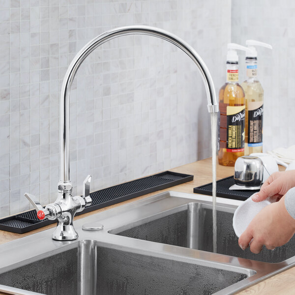 A person using a Waterloo deck mount faucet to wash dishes in a sink.