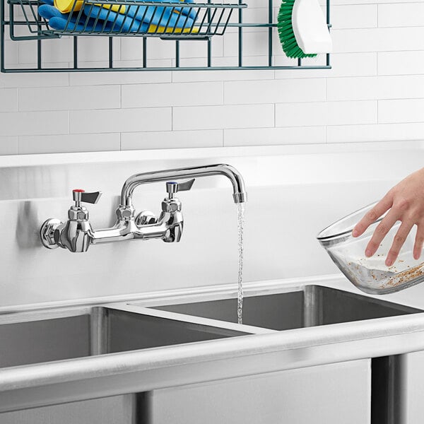 A hand pouring water from a Waterloo wall-mounted faucet into a sink.