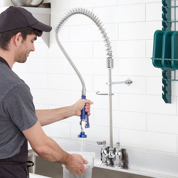A man in a black shirt and hat using a Waterloo pre-rinse faucet to wash a blue metal bar with a hose.