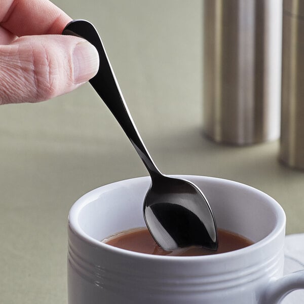 A person holding an Acopa Vernon stainless steel demitasse spoon in a cup of liquid.