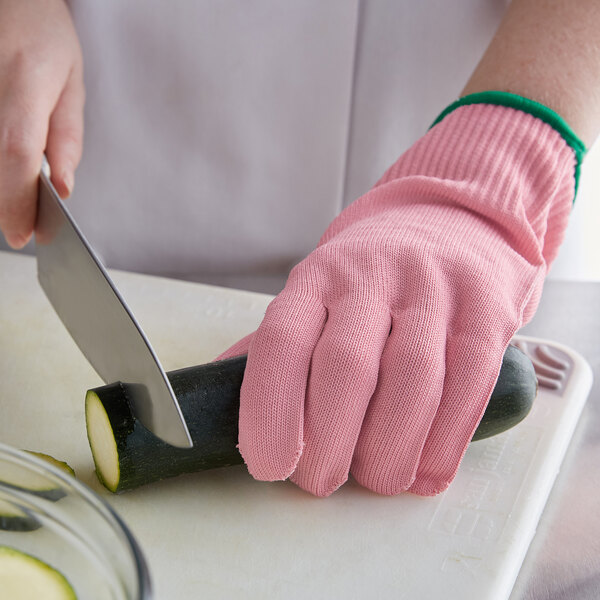 A person wearing Mercer Culinary pink cut-resistant gloves cutting a zucchini with a knife.