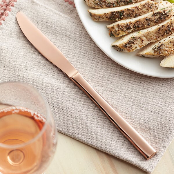 An Acopa Phoenix rose gold stainless steel forged dinner knife on a plate of meat.