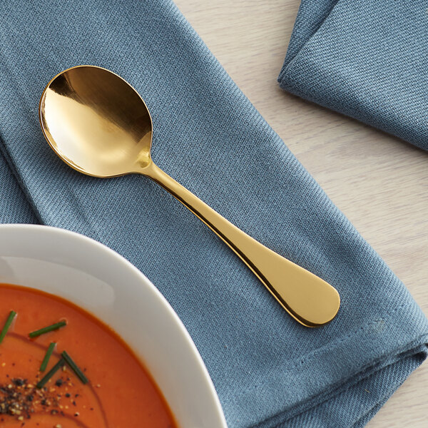 An Acopa Vernon stainless steel bouillon spoon in a bowl of soup on a table with a napkin.