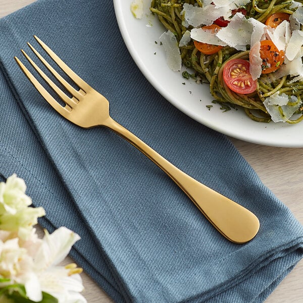 An Acopa Vernon stainless steel dinner fork with a gold handle on a blue plate of food.
