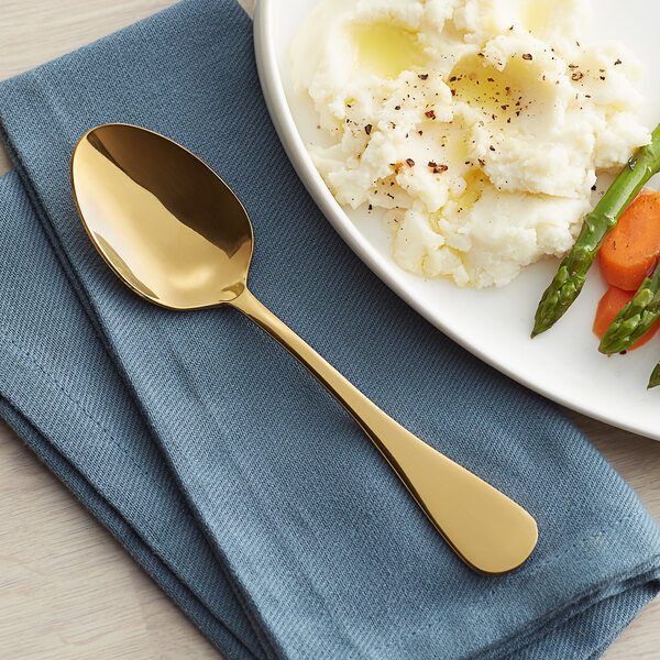 A plate with mashed potatoes, carrots, and a Vernon Gold stainless steel oval bowl dinner/dessert spoon on it.