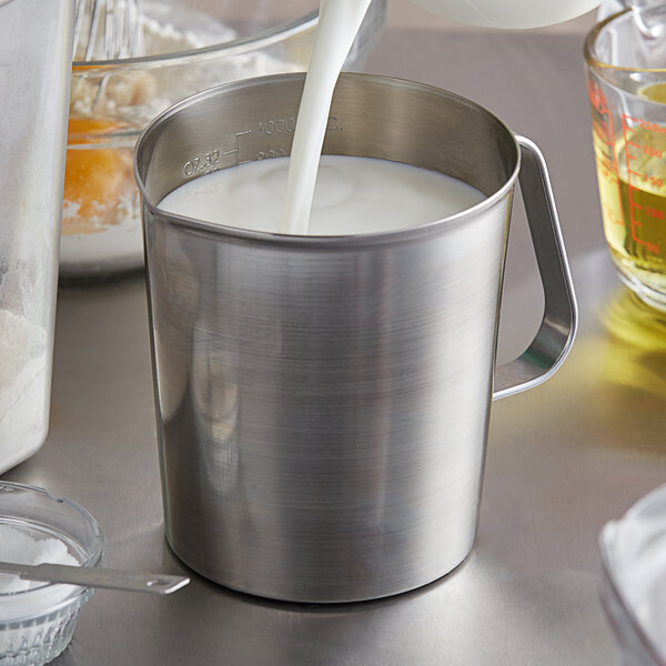 A close-up of a Vollrath stainless steel measuring cup with milk being poured into it.