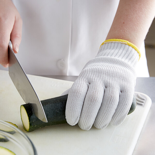 A person wearing Mercer Culinary Millennia cut-resistant gloves cutting a zucchini with a knife.