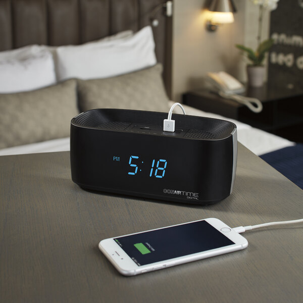 A black Conair digital alarm clock with a white phone charging on it.