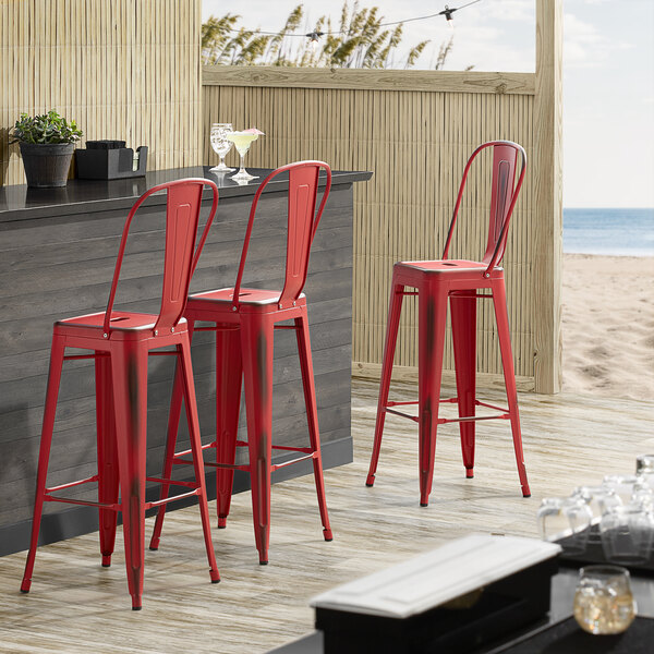 Lancaster Table & Seating Alloy Series Distressed Red Metal Indoor / Outdoor Industrial Cafe Barstool with Vertical Slat Back and Drain Hole Seat