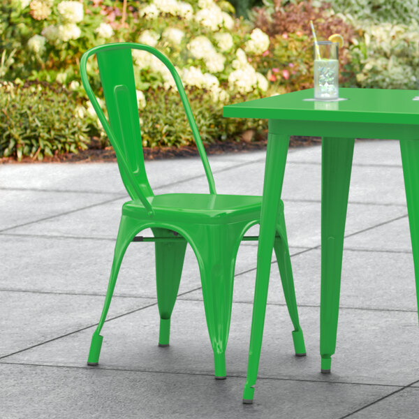 A green Lancaster Table & Seating outdoor cafe chair on a stone patio with a table.