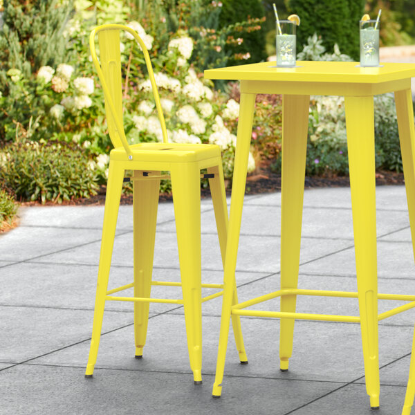 A yellow Lancaster Table & Seating outdoor cafe barstool on a patio.