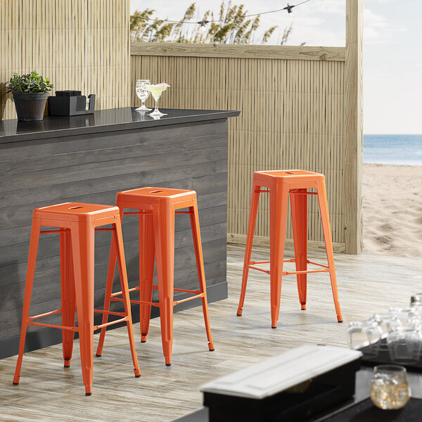 Lancaster Table & Seating Alloy Series Orange Stackable Metal Indoor / Outdoor Industrial Barstool with Drain Hole Seat