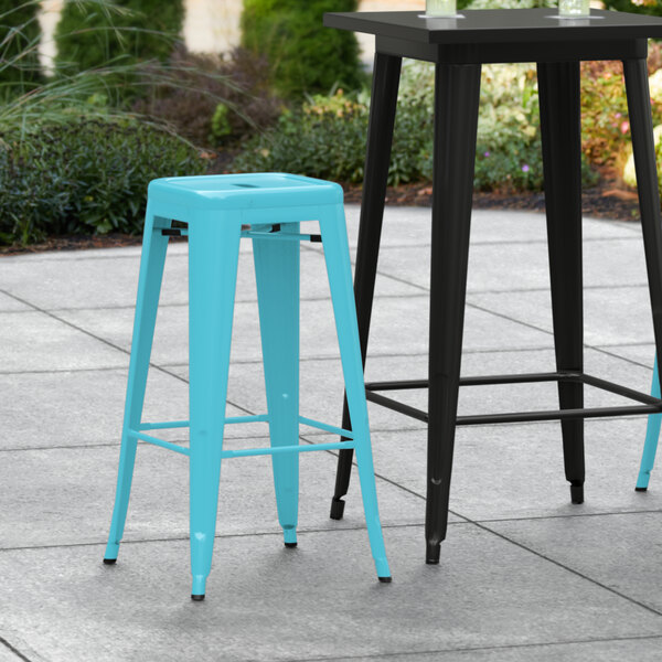 Two blue Lancaster Table & Seating outdoor barstools on a patio.