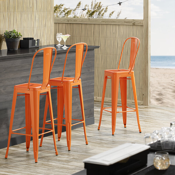 Lancaster Table & Seating Alloy Series Orange Metal Indoor / Outdoor Industrial Cafe Barstool with Vertical Slat Back and Drain Hole Seat