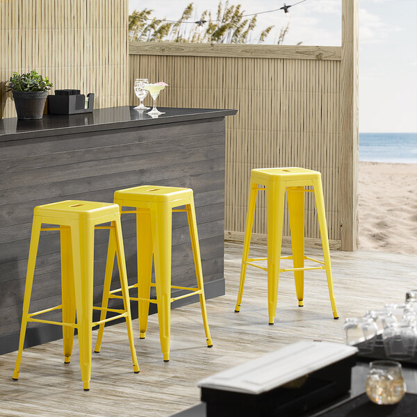Lancaster Table & Seating Alloy Series Yellow Stackable Metal Indoor / Outdoor Industrial Barstool with Drain Hole Seat