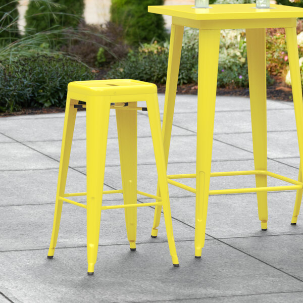 A yellow Lancaster Table & Seating outdoor barstool on a patio.