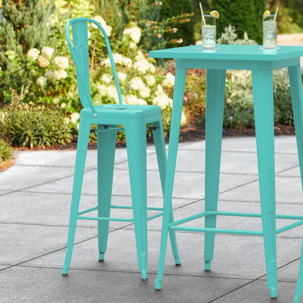 A Lancaster Table & Seating seafoam outdoor barstool on a table on a patio.