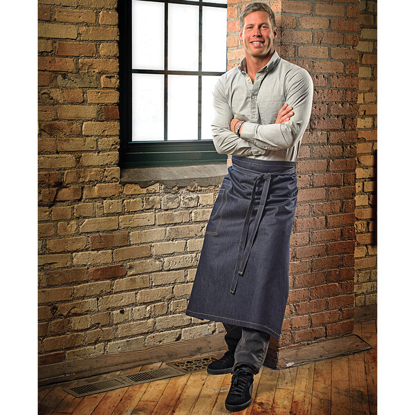 A man wearing a Mercer Culinary indigo denim bistro apron with 2 pockets.