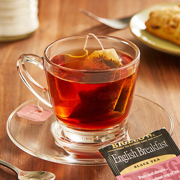 A glass cup of Bigelow English Breakfast Tea with a tea bag on a saucer.