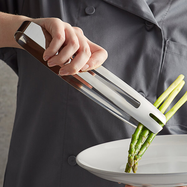 A person using Vollrath stainless steel serving tongs to pick up asparagus.