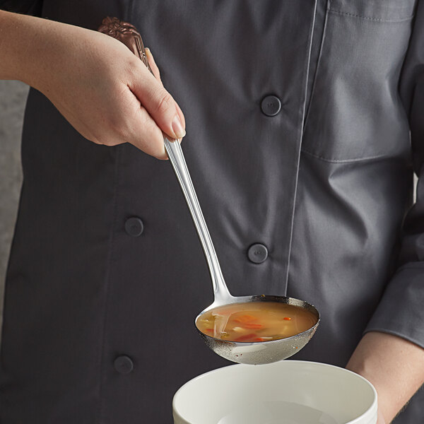 A person using a Vollrath stainless steel ladle to serve soup