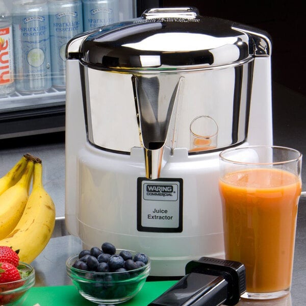 A Waring juice extractor on a counter with a glass of orange juice.