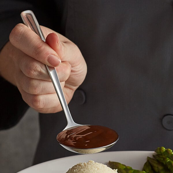 A person using a Vollrath stainless steel ladle to pour chocolate sauce over a plate of food.